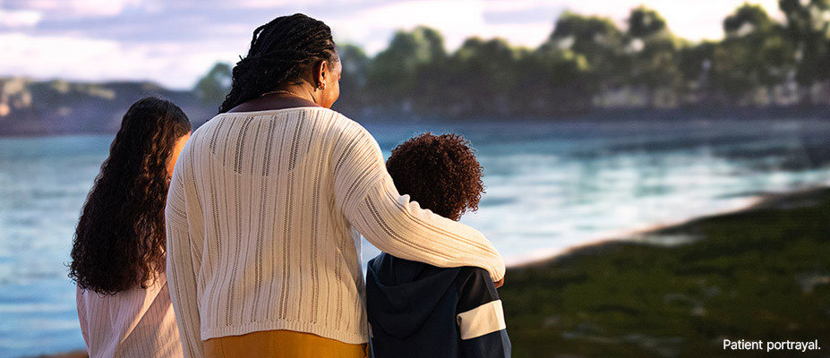 A woman and two children stand together looking at a lake.