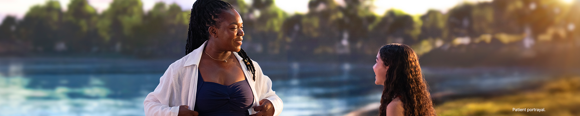 A woman chats with a child in front of a lake.
